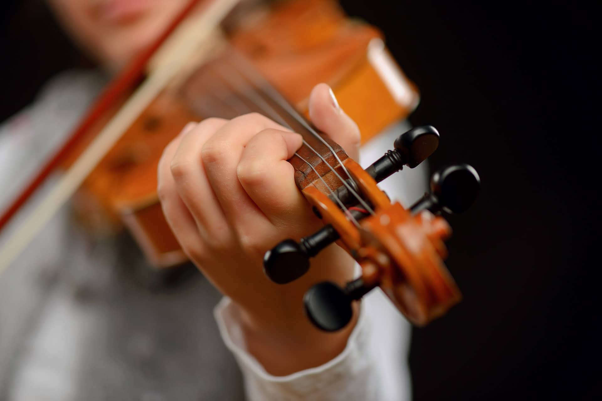 Revel in the sound. Close up of professional violin in hands of little girl holding it and playing while standing isolated on black background